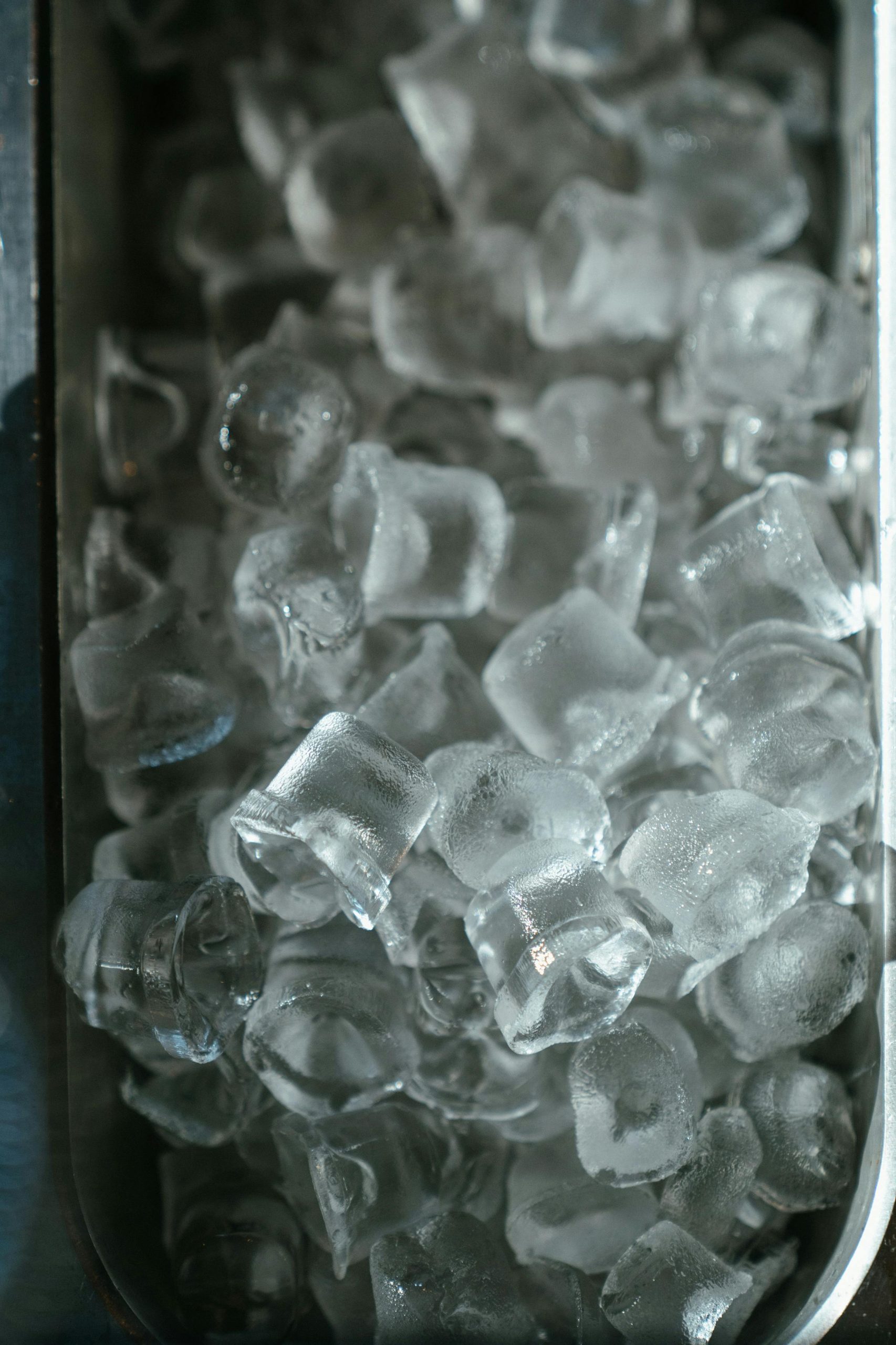 A detailed view of crystal clear ice cubes in a metal tray, perfect for refreshing drinks.